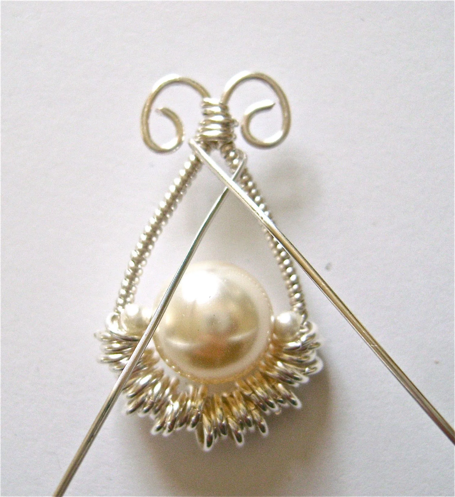 step 10 - Cut another piece of half round wire to measure 4”. Place the middle of the wire with the flat side against the spot below the center wraps. Fold the wires to the back of the work and bring them back to the front crossing each other.