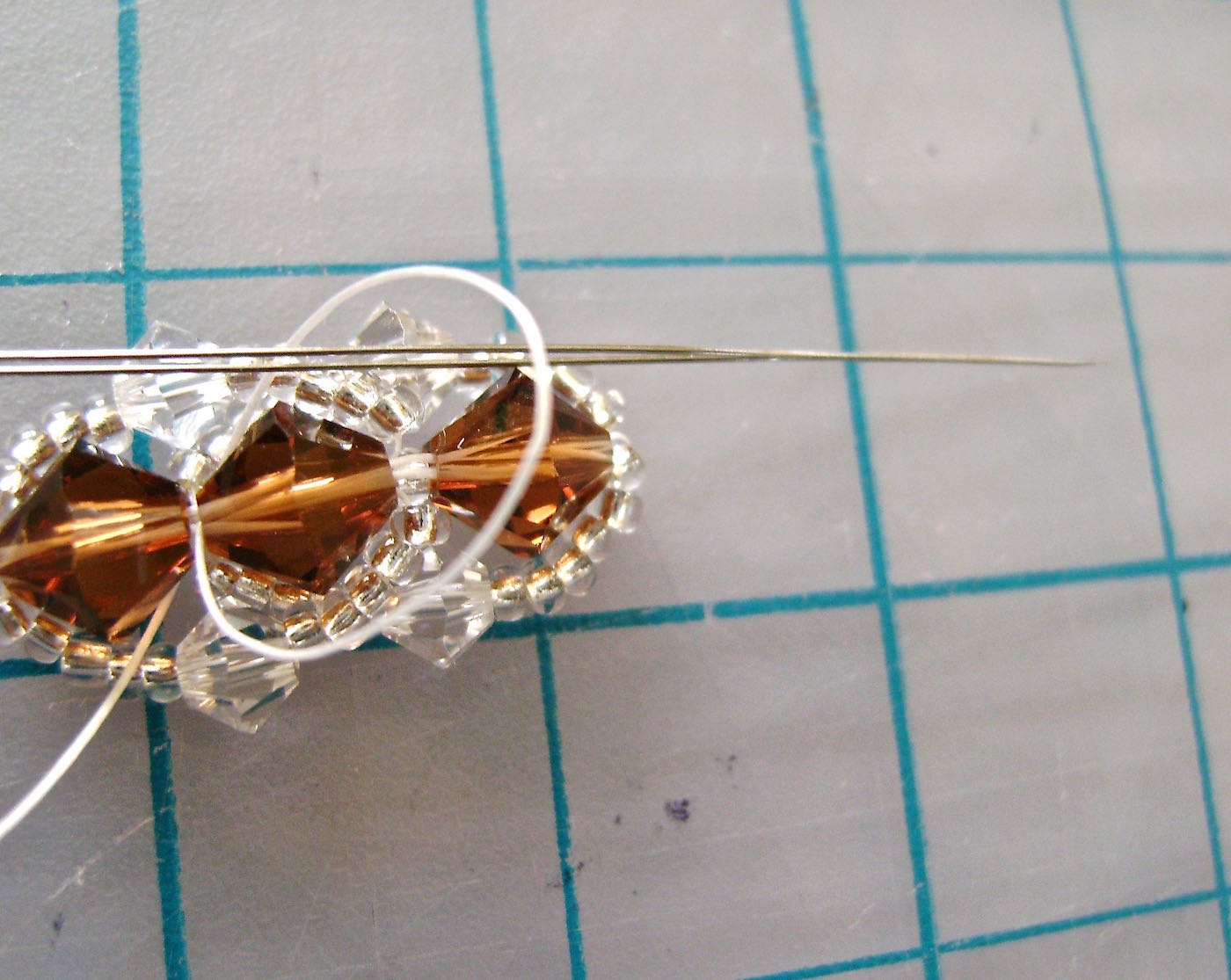 step 11 - Push the needle through the loop and pull to secure the knot which should be hidden between the two 6MM beads. Finish by either: 1) taking the needle through more sets of 6MM beads, creating 2 - 3 more knots, or 2) taking the needle back through the end beads, through the clasp and back up through the beads before knotting again. It’s a personal choice. The second option will create a double hold on the clasp. Cut off the excess thread with nippers or sharp pointed scissors. Finish the other end of the bracelet following steps eight through eleven.
