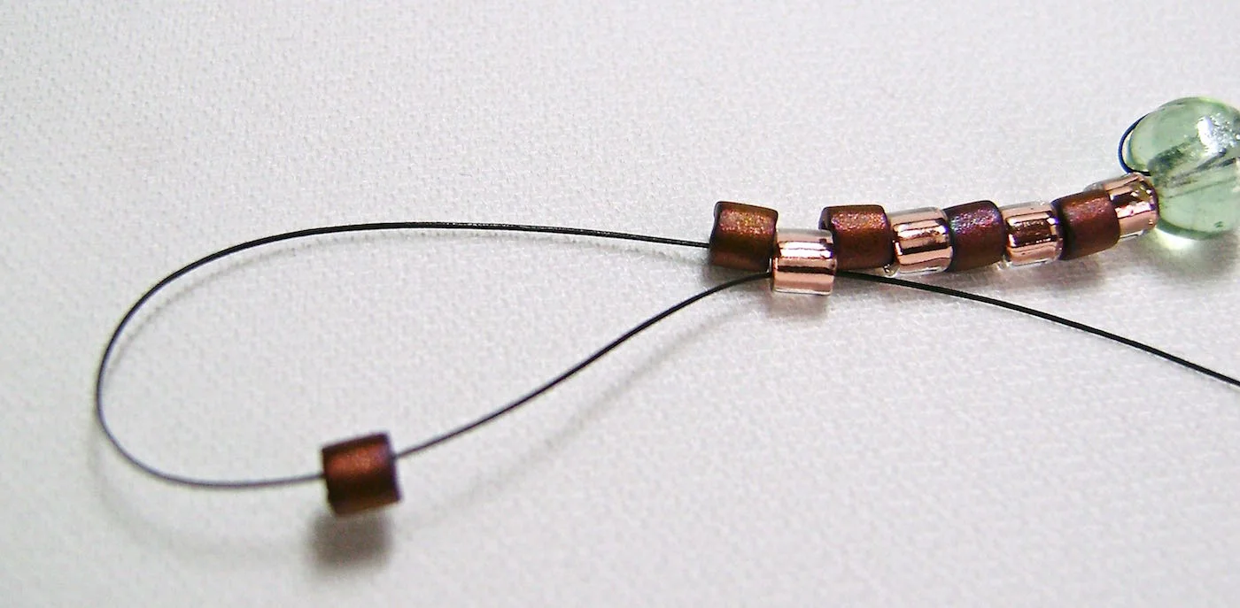 step 3 - At the end of the row, add one more dark bead which will be the base of the next row. Pass your needle through the first light bead of the previous row. Pull the thread through but don’t worry too much about the look of things at this point. By the time you finish this row you will see a pattern emerging.