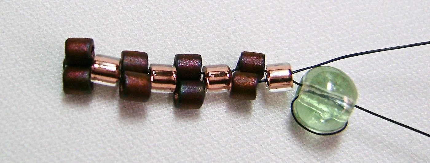 step 6 - Finish the row by adding another dark bead and passing through the fourth light bead. You have finished a complete row and should notice that what you’re creating is a design with four beads that drop down from the previous work. This will happen with each row you complete. 
