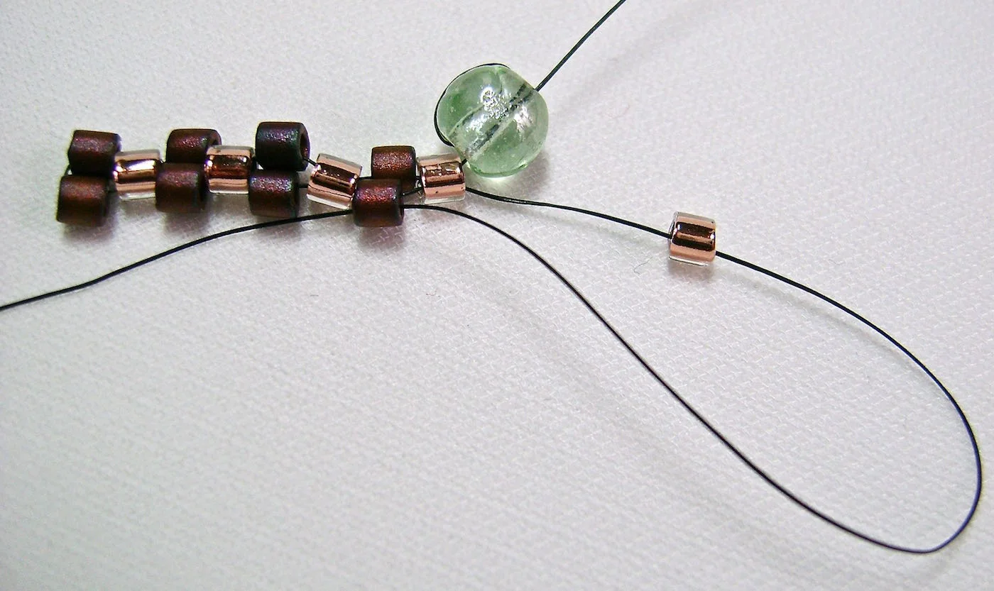 step 7 - Thread on a light bead to begin the next row. In this row you will be adding light beads, passing the needle through the dark beads of the previous row. You continue to alternate from light beads to dark in each row until your reach the length bracelet you need. This is the entire magic of the peyote stitch. If you’re ever unsure of what color bead you should be adding at the end of the row, look at the color of the bead on that side of the bracelet. Because you’re designing with an even number of beads, the strip of beads on one side of the bracelet will be the opposite of the beads on the other.