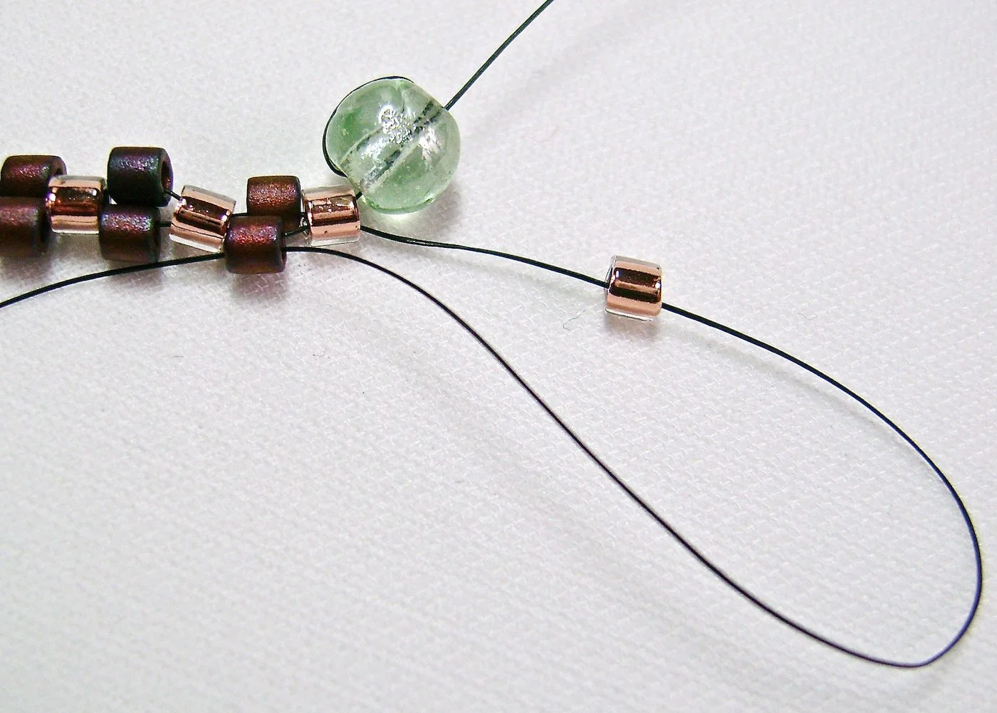 step 6 - Thread on a bead to begin the next row working from right to left. In this and the remainder rows you will be adding three beads and passing the needle through the dropped beads of the previous row. This is the entire magic of the peyote stitch.