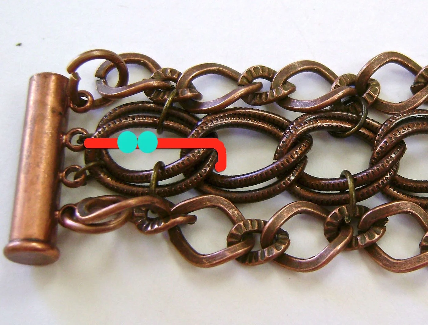 step 8 - Tie a length of beading cord to the center double links closest to the clasp. The cord should be twice the length of your bracelet. Make a couple of knots on the bracelet backside to secure it and dot it with glue. String on two glass beads and move the cord from left to right following the red line in the photo. Move over the first joint of the links.