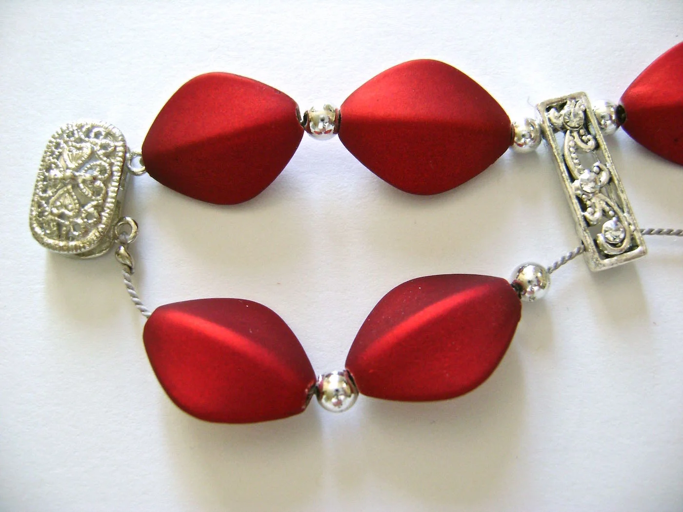 step 8 - Add silver and red beads. Slide the needle through the bottom holes of the spacer bar and continue adding beads until the bottom row matches the top row. To complete the bracelet, attach the cord to the clasp and secure with a crimp bead.