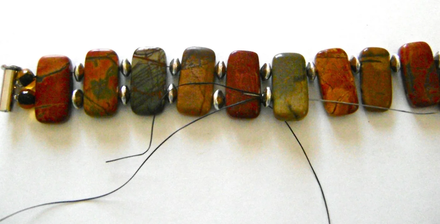 step 8 - Move through the needle through the bottom holes of the stone beads adding spacer beads between them. Slip the needle through a round bead, through the bottom hole of the clasp, back through the round bead.