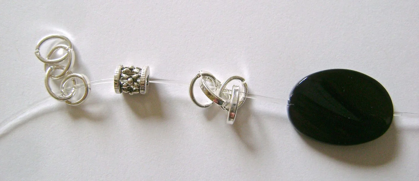 step 4 - Add a barrel bead. Pass the cord through all four links in another chain piece. Add a black bead to the cord.