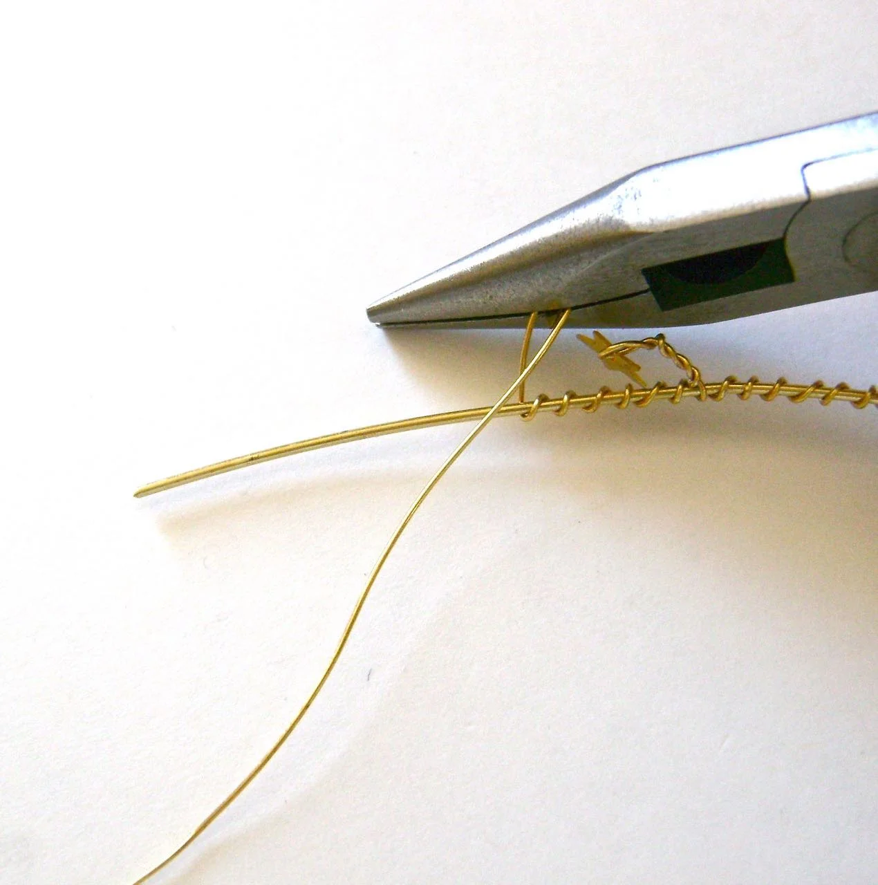 step 6 - Grasp the bend in the wire with pliers and twist the work 4 or 5 times to secure the star. Wrap the wire around the core wire 7 times. Create another bend. Add stars and wire to the core wire in this manner until all but about an inch of the wire is wrapped.