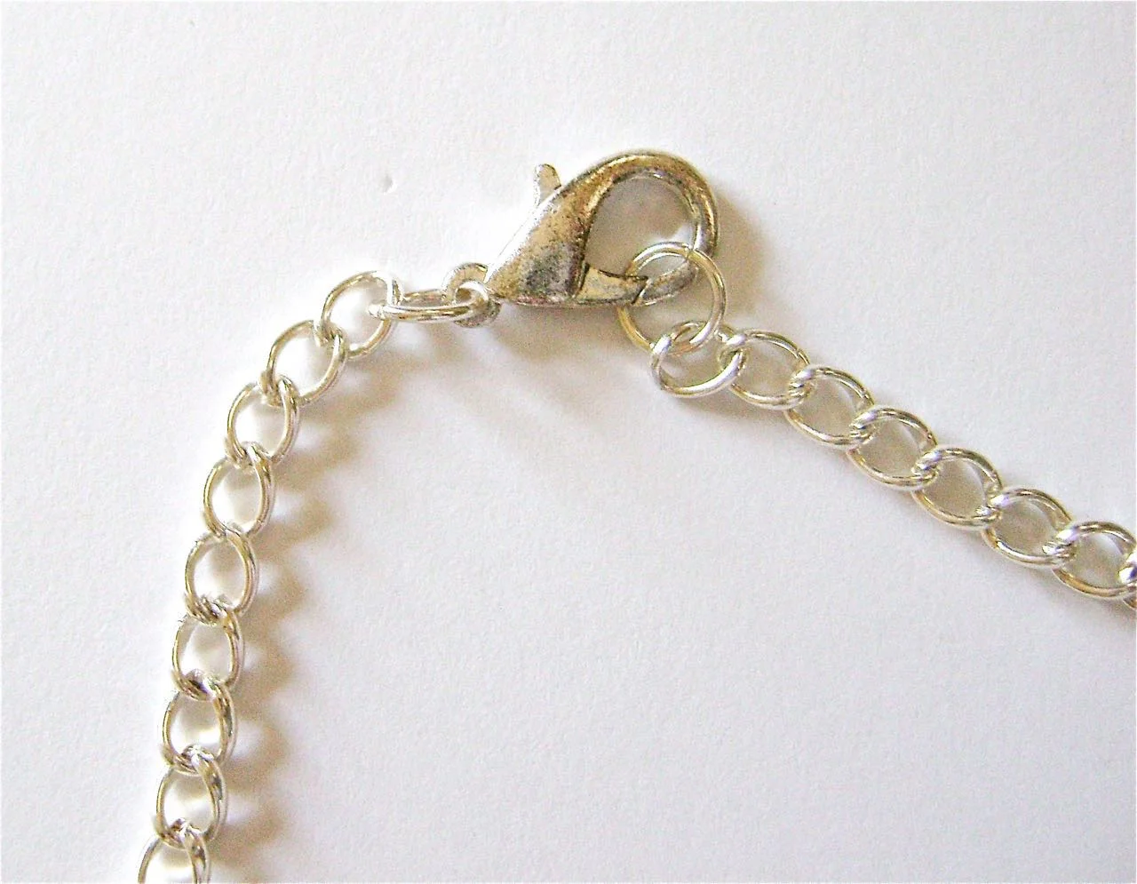 step 15 - Attach a 5.5” length of chain to the hook of each clam shell. Attach a lobster clasp to the end of one chain and a jump ring to the other.