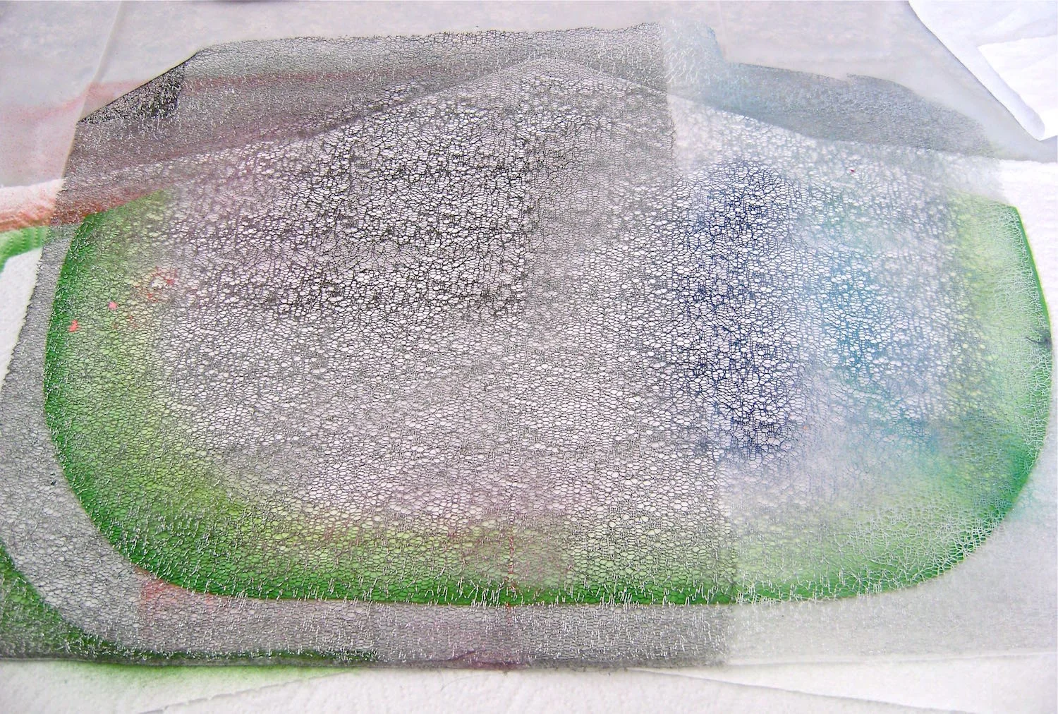 step 9 - Remove the template and lay a piece of cheesecloth or other netted type fabric across the mat. Mix pink and orange paint to achieve the watermelon color. Hold a waded tissue over the rind area to protect it as you airbrush the surface. Reposition the tissue unevenly around the mat as you paint.