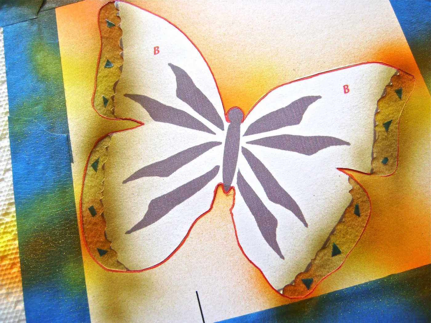 step 8 - With regular scissors, cut a few tiny odd shapes from painter’s tape and adhere them to the exposed wing borders. Paint the borders with a light spray of Bronze Have More Fun paint.
