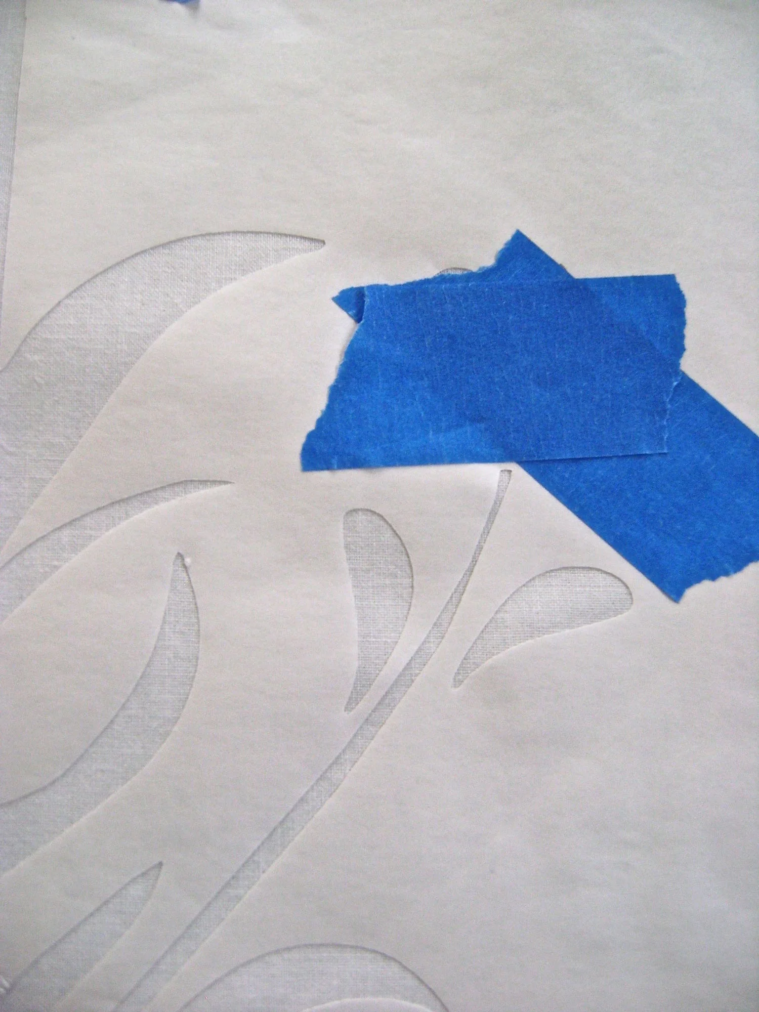 step 6 - With a dry iron set on “cotton”, press the Freezer Paper to the white fabric. Be sure all design edges adhere to the fabric. Place painters tape over the flowers.
