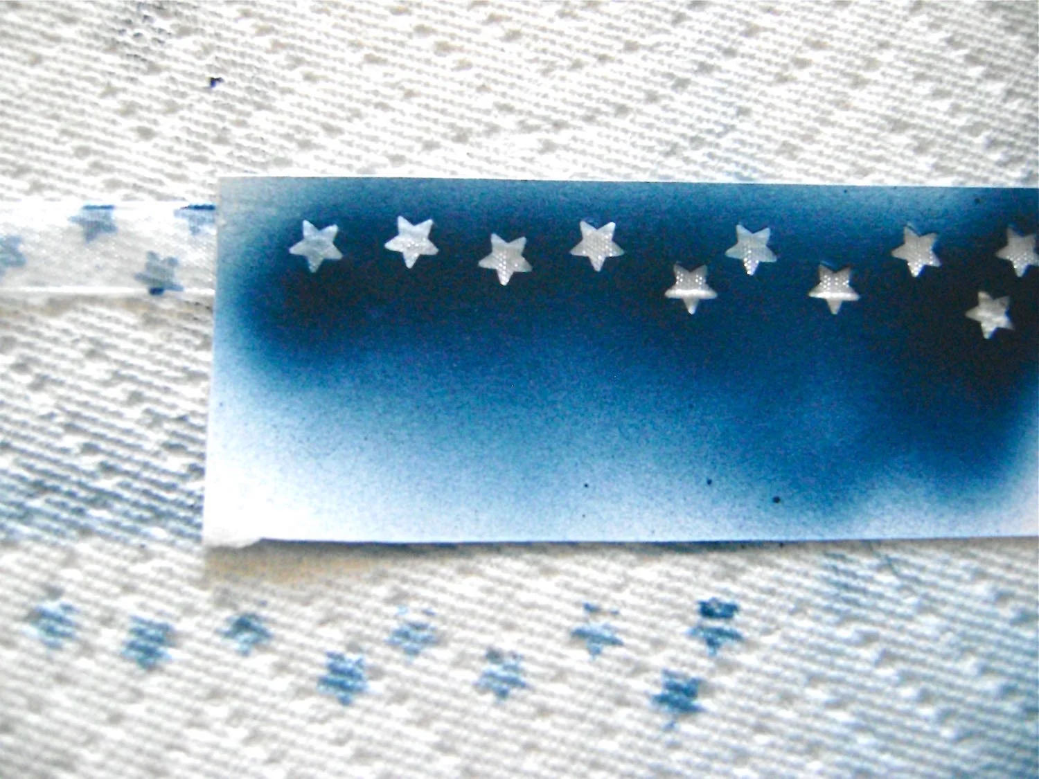step 3 - Spray the back of the strip with repositionable stencil spray. Press it on the sheer, white ribbon and spray with Blue Angel paint. Move the stencil along the ribbon, spraying with paint until the entire length is covered with tiny stars.