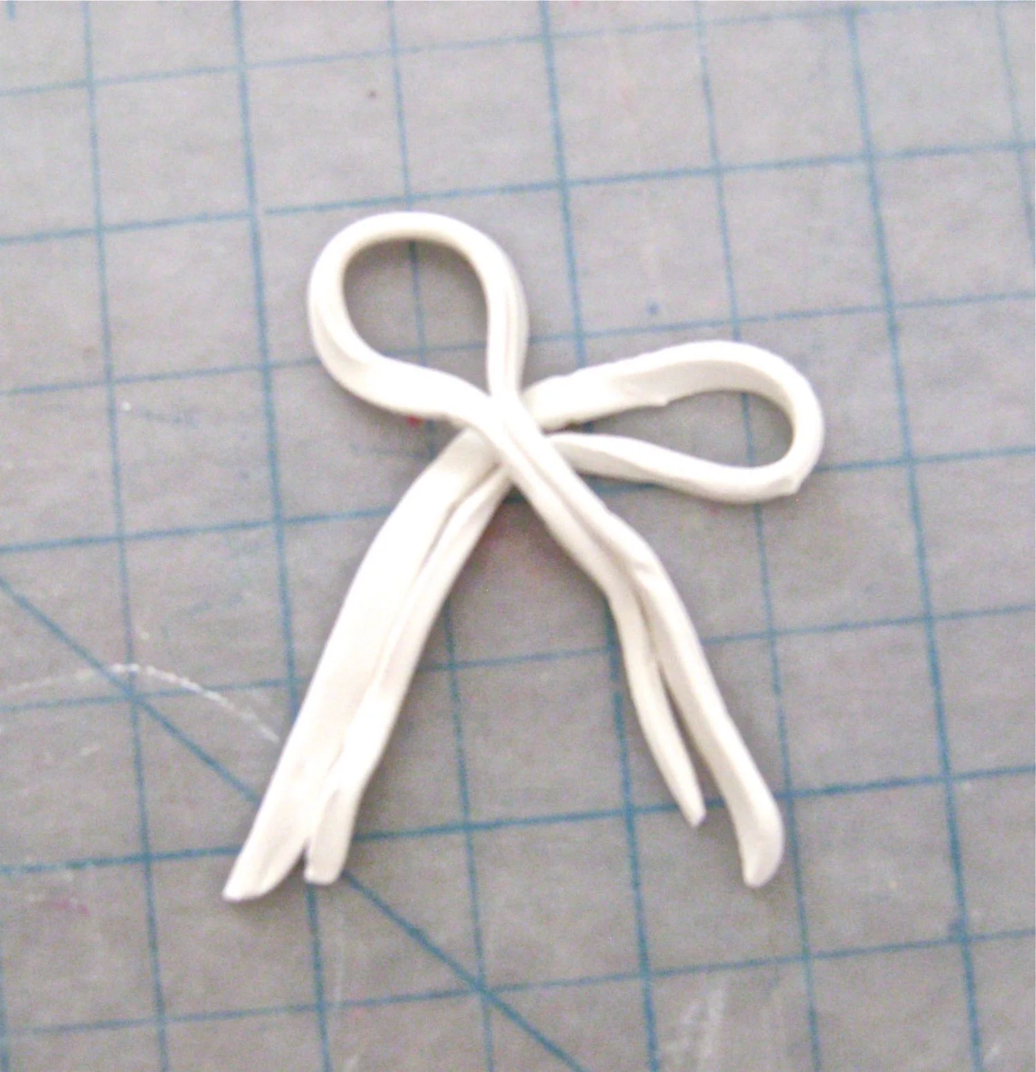 step 14 - Roll out two pieces of clay, cut them into narrow strips and fold them to form the bow. Wrap another small piece of clay around the strips to create the center of the bow. Press it in place on the teddy bear.