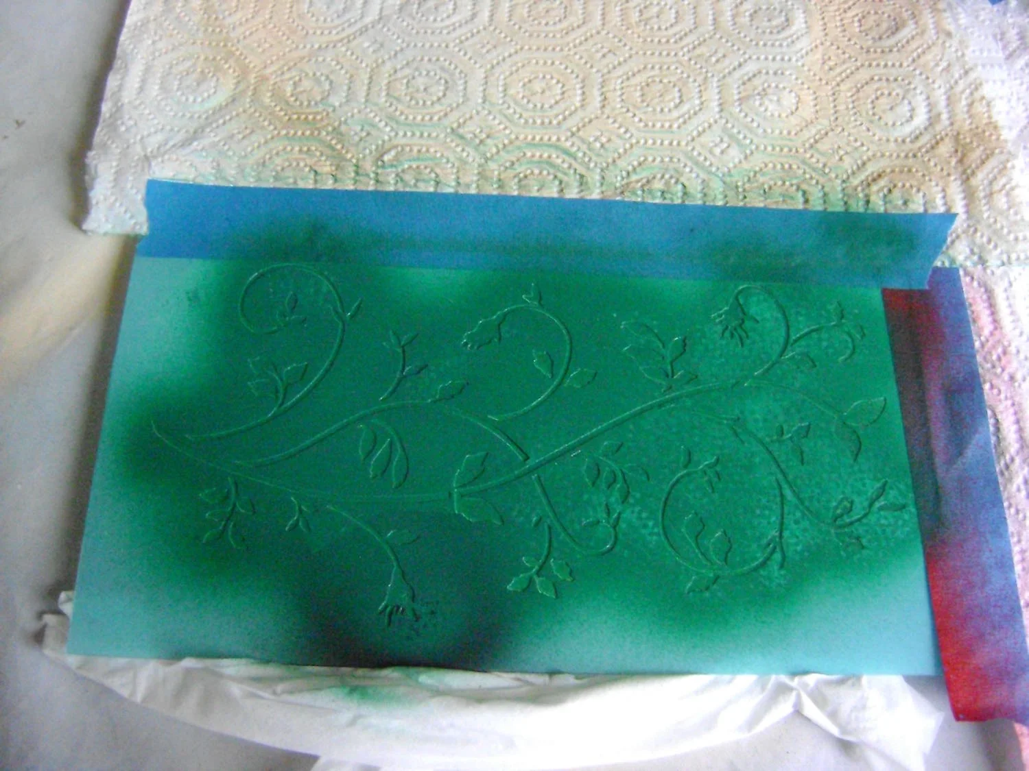 step 9 - Spray the back of the floral stencil with adhesive. Place it across the painted plaque. Airbrush it with green paint mixed with a bit of red to deepen the color. Allow to dry then remove the stencil. 