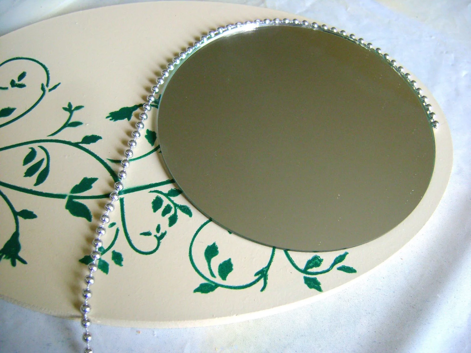 step 13 - Also glue a string of silver beads around the mirror. Use small dots of the hot glue along the rim, holding each section of beads in place until set.
