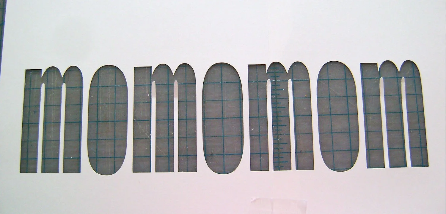 step 2 - Use a craft knife or stencil cutting machine to cut out the Mom stencil. Be sure to save the center of the “O”s. Spray the back side of the pieces and stencil with Spray Mount adhesive.