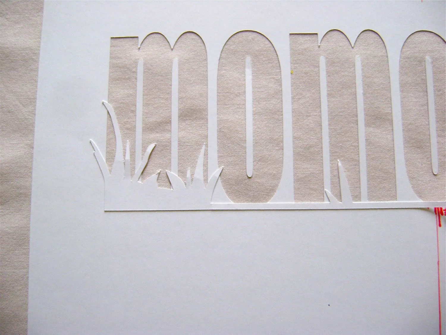 step 5 - Apply Spray Mount adhesive on the back of the die cut grass piece. Center, align, and press the piece onto the Mom stencil. The bottom edge of the grass piece should be flush against the bottom of the Mom lettering.