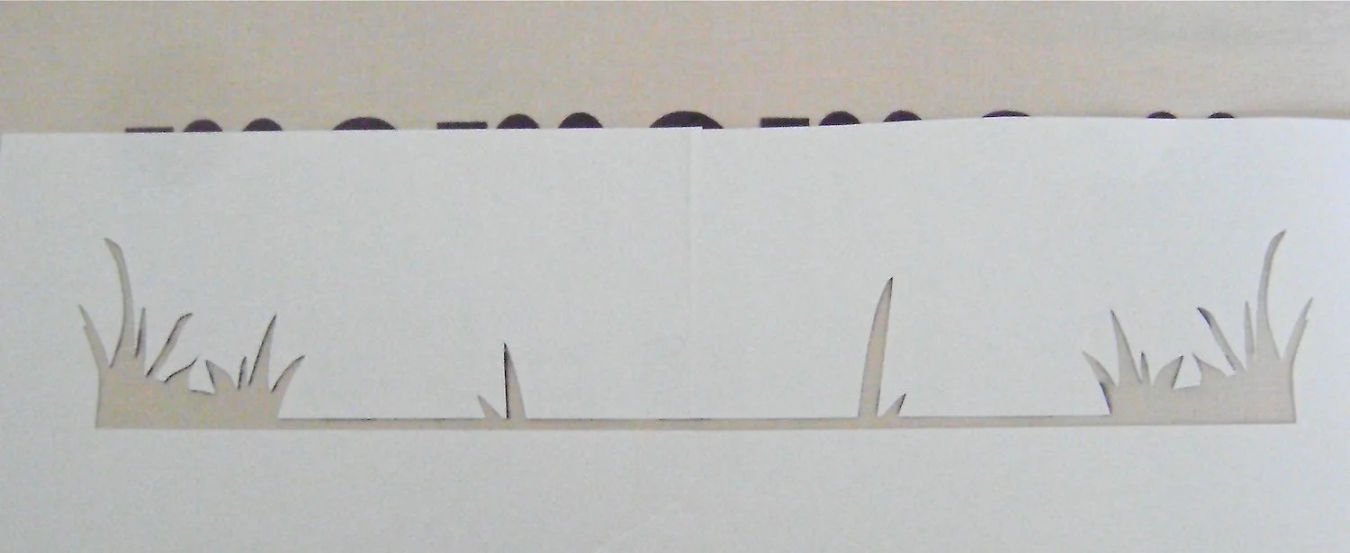 step 8 - Apply Spray Mount adhesive on the back of the grass stencil. Matching the shape created by the die cut outline, align the stencil and press it to the fabric.