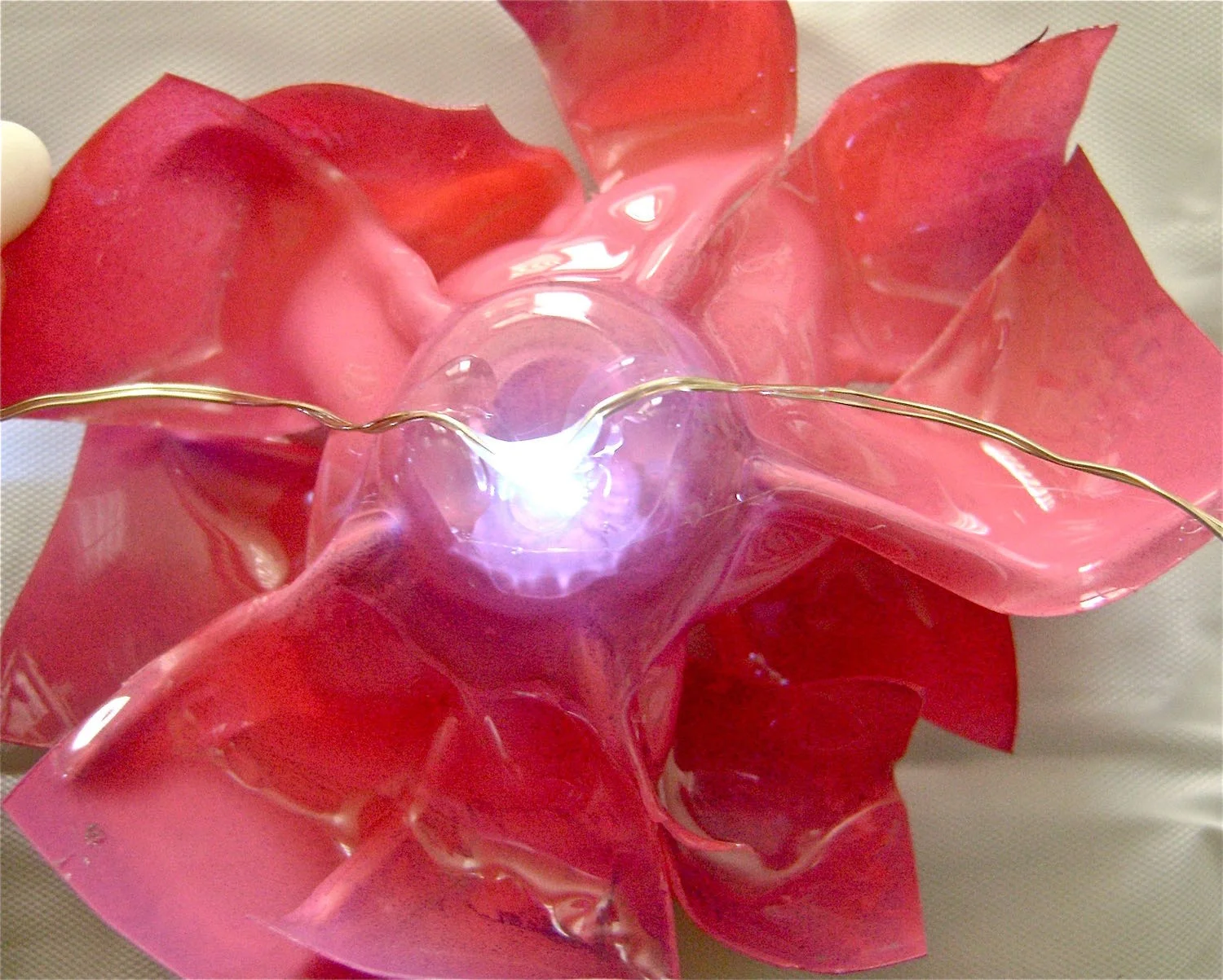 step 8 - Position a flower under the second bulb in the light string. Apply hot glue to the left and right of the center. Don’t apply glue to the very center, as it will block the light. Press the cords of the light string onto the hot glue. Continue attaching flowers on every third bulb.