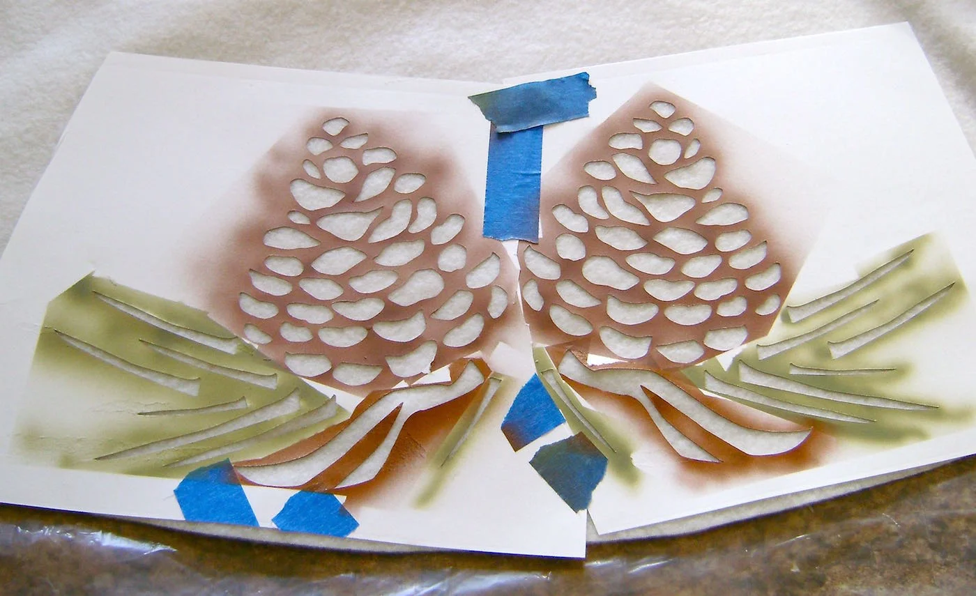 step 9 - Overlap the two stencils to form one large stencil, tilting the images slightly to match the pine cone positions in the skirt photo. Cut around open areas that are blocked by the overlap. Center the stencil on one of the skirt pieces with the bottom edges of the image one-inch from the bottom of the skirt. 