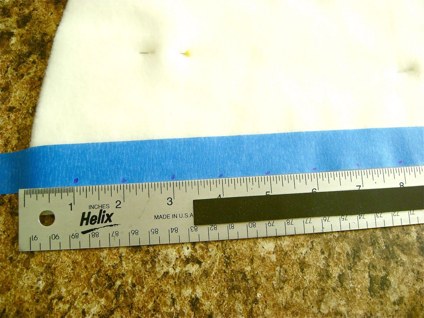 step 15 - Place a strip of painters tape 3/8 “ from the straight edge. Position a yardstick beside the tape and mark the tape at one-inch increments. Start one inch from the skirt bottom. Add one extra mark at 23.5”. Pinning the two skirt pieces together will prevent them from shifting during handling.
