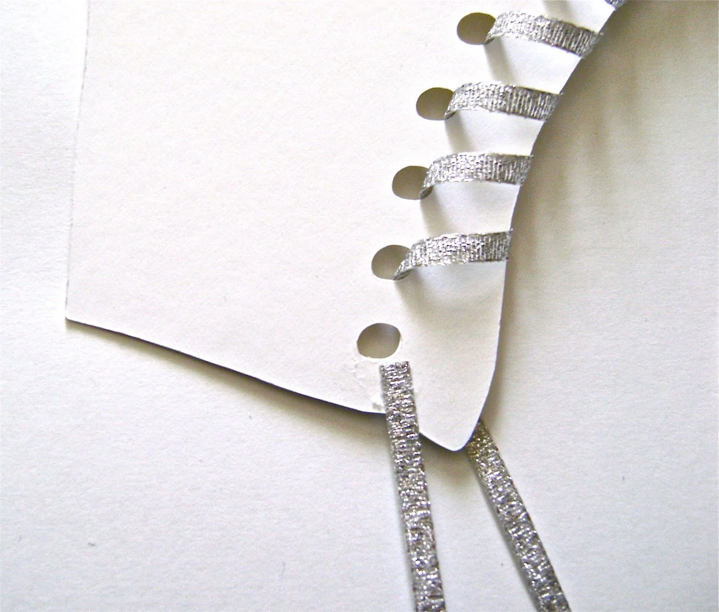 step 5 - When the ribbon is secured to the wrong side, flip the skate over and thread the ribbon through all the holes in the skate except the first one at the top. Turn the skate over and glue the 11” piece of ribbon to the card stock above the first hole. Set aside.