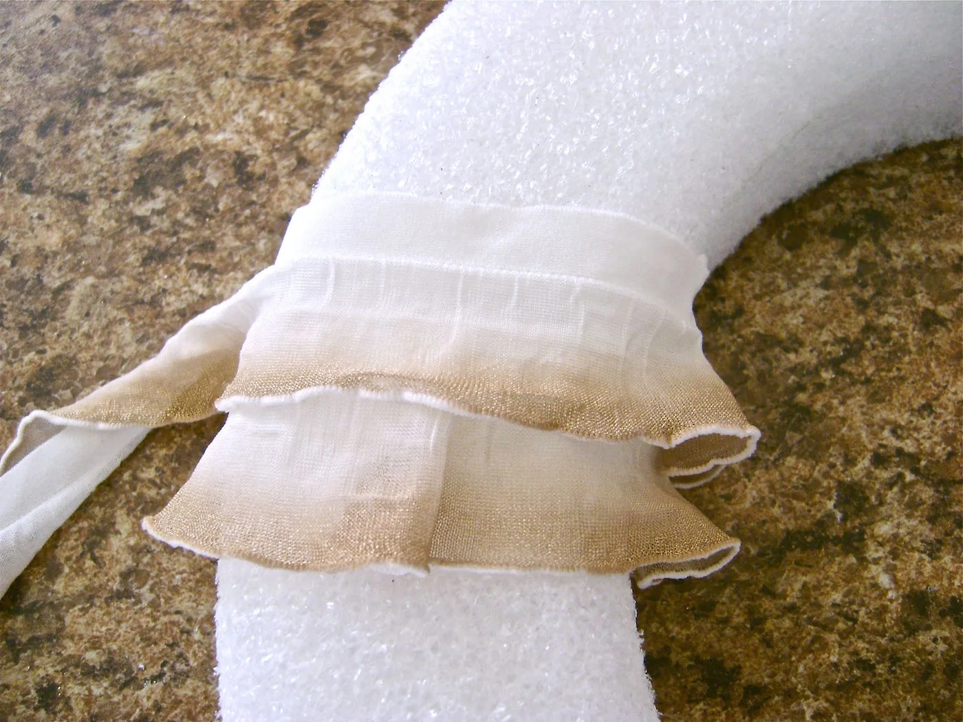 step 6 - Bring the fabric to the back of the wreath and start your next row. The ruffle hem from the previous row should cover the flat border of the new row when it is glued in place.
