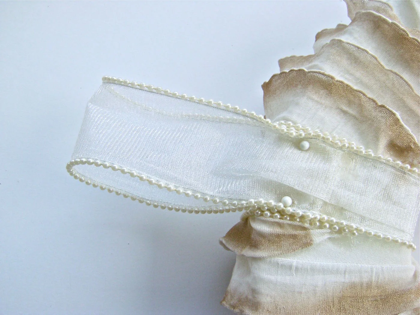 step 8 - Add The Ribbon and Holiday Stems Wrap a piece of pearl edged ribbon over the flat double border, bringing it to the back of the wreath. Fold the ribbon, creating a 6” loop. Slip the raw edge of the ribbon against the wreath and use straight pins to hold it in place. Dab hot glue on the pins before inserting them into the wreath.