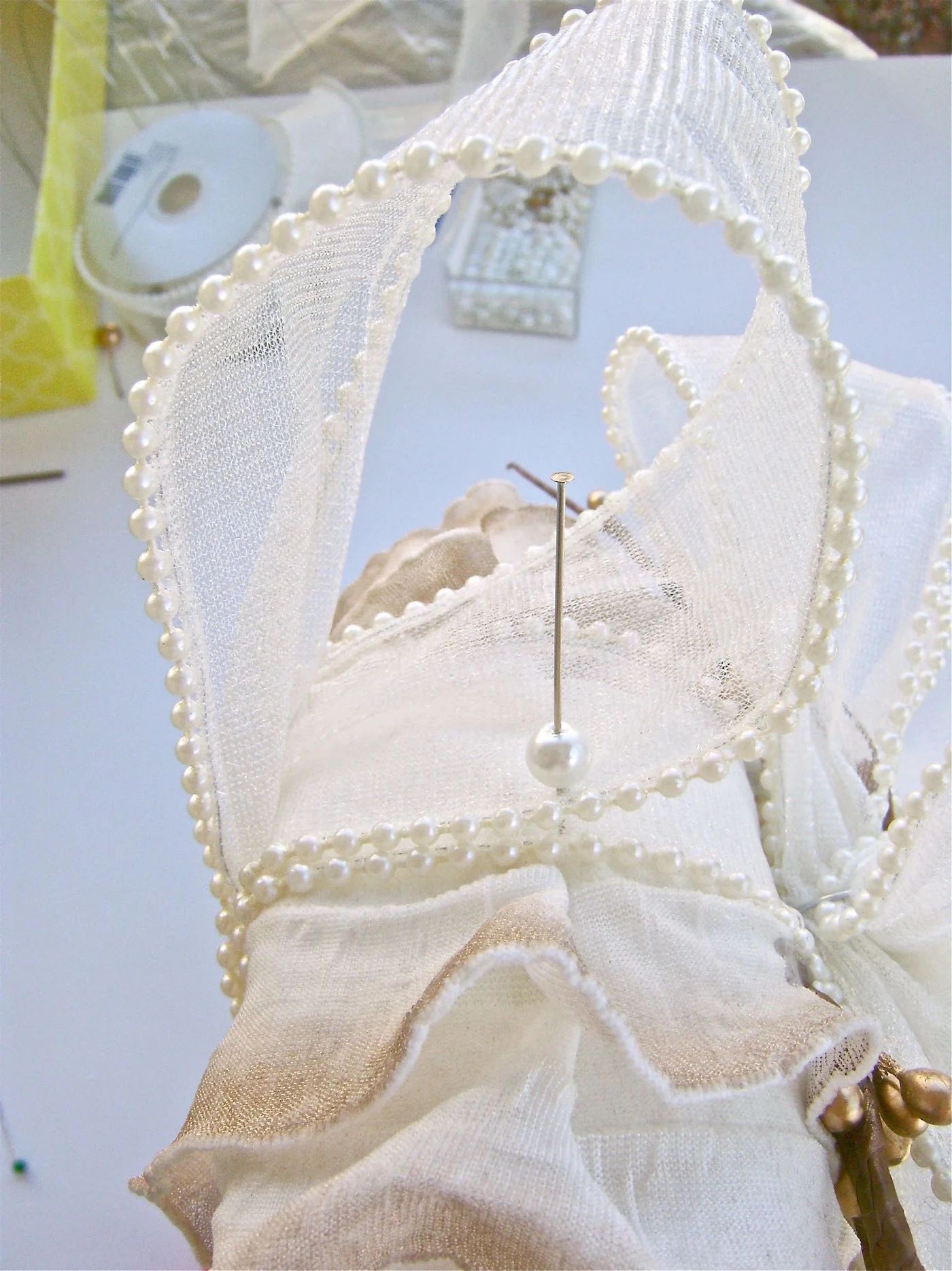 step 14 - Finish the wreath by securing the loop you made at the back of the wreath, to the top center of the wreath. Put nail head wires through a pearl, dab the wire with glue and push it into the Styrofoam at the left edge of the ribbon. Repeat on the right side. Attaching the ribbon to the center will allow the wreath to hang properly.