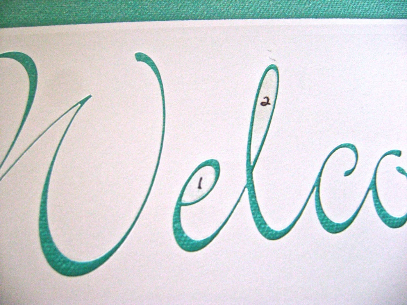step 3 - I used a stencil cutting machine to cut out the welcome message on card stock and repositionable spray adhesive to attach it to the canvas. If you don’t have a machine and don’t want to cut the stencil by hand, print out the message and transfer the words to the canvas using tracing paper. Paint over the letters with mocha paint using a fine brush.