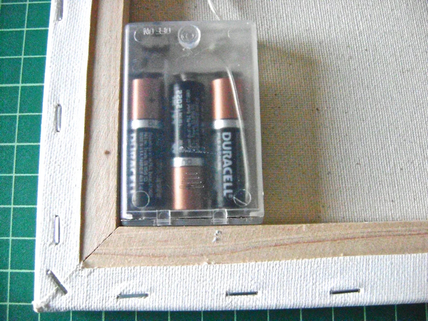 step 12 - Fill the battery pack then tuck it into the lower corner of the canvas’ wood frame. It should be recessed so it will not interfere if the canvas is hung flush to the wall. Hot glue it in place. Be sure the control switch is in a convenient position.