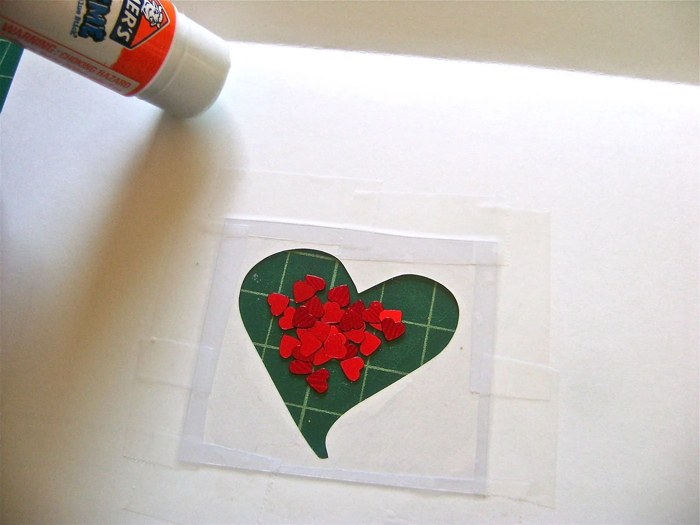 step 5 - With a glue stick, trace around the heart shape on the plastic. Also use the glue stick to trace the edges of the bottom half of the card and close to the fold. Cut a new sheet of card stock in half and press it to the glued page, aligning the edges. Press around the heart which will adhere the card stock to the plastic and create a pocket for the hearts. Allow the glue to set.
