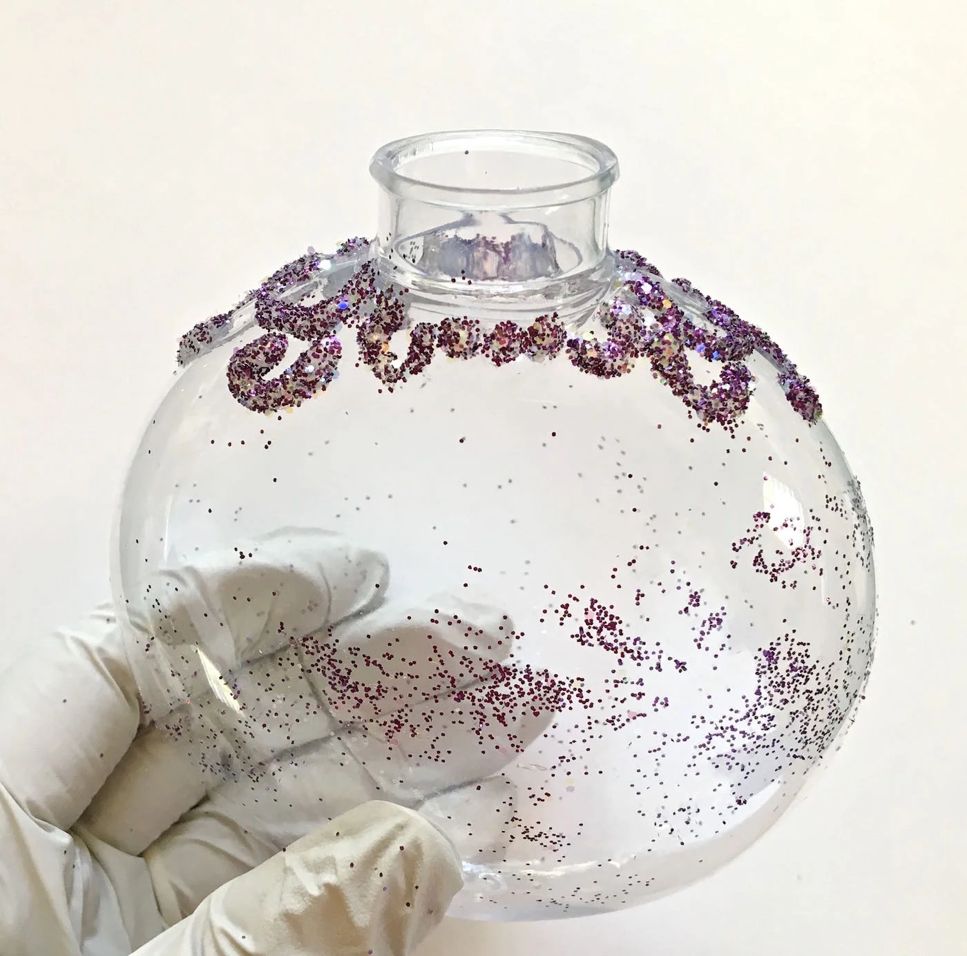 step 3 - Create curls at the top of the ornament with the nozzle of the glue container. Sprinkle purple glitter on the glue. Shake off excess and allow it to dry thoroughly.