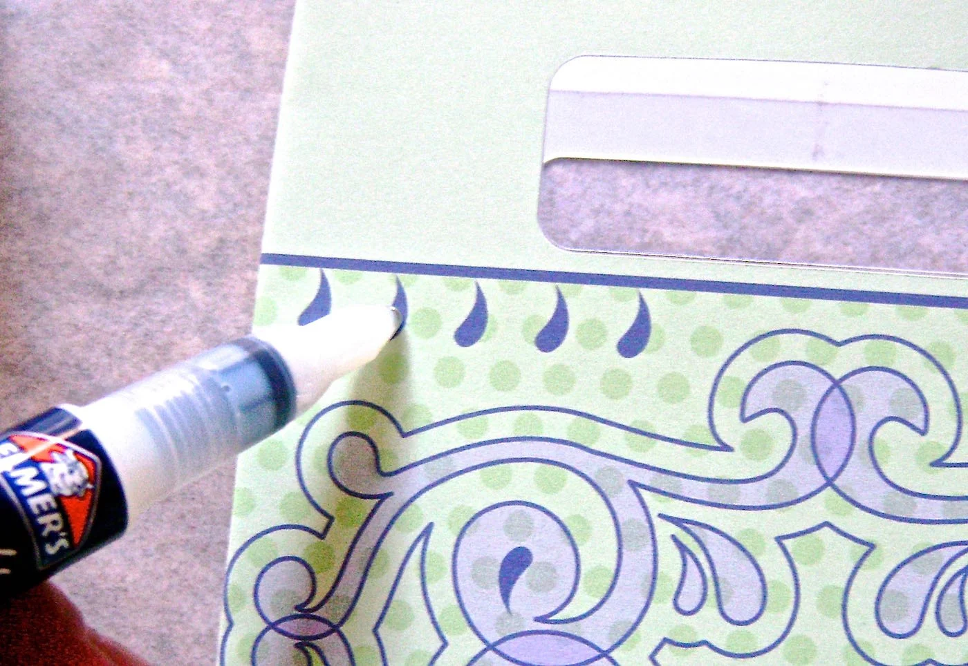 step 14 - Finish the bag by applying glue with a glue pen to the lilac teardrop shapes. Press down on the pen to deposit glue on the round end of the drops then drag the glue to the pointy end. Sprinkle the glue with glitter.