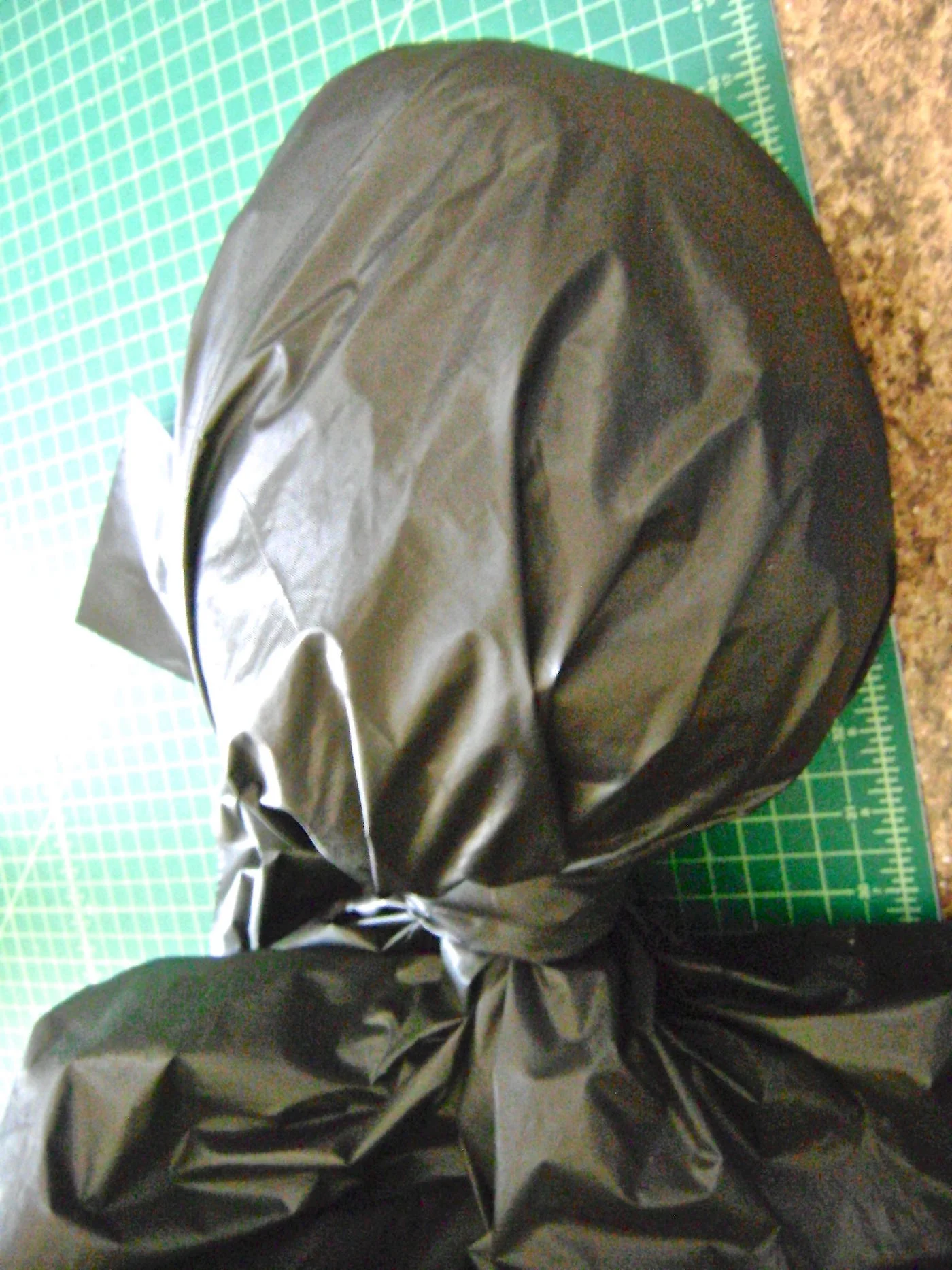 step 9 - Using the first table cover, cut three two-inch wide strips of plastic to measure 18” long. Open up a second plastic table cover and place the center of it over the center top of the head. Gather it at the neck and secure it with a plastic strip.