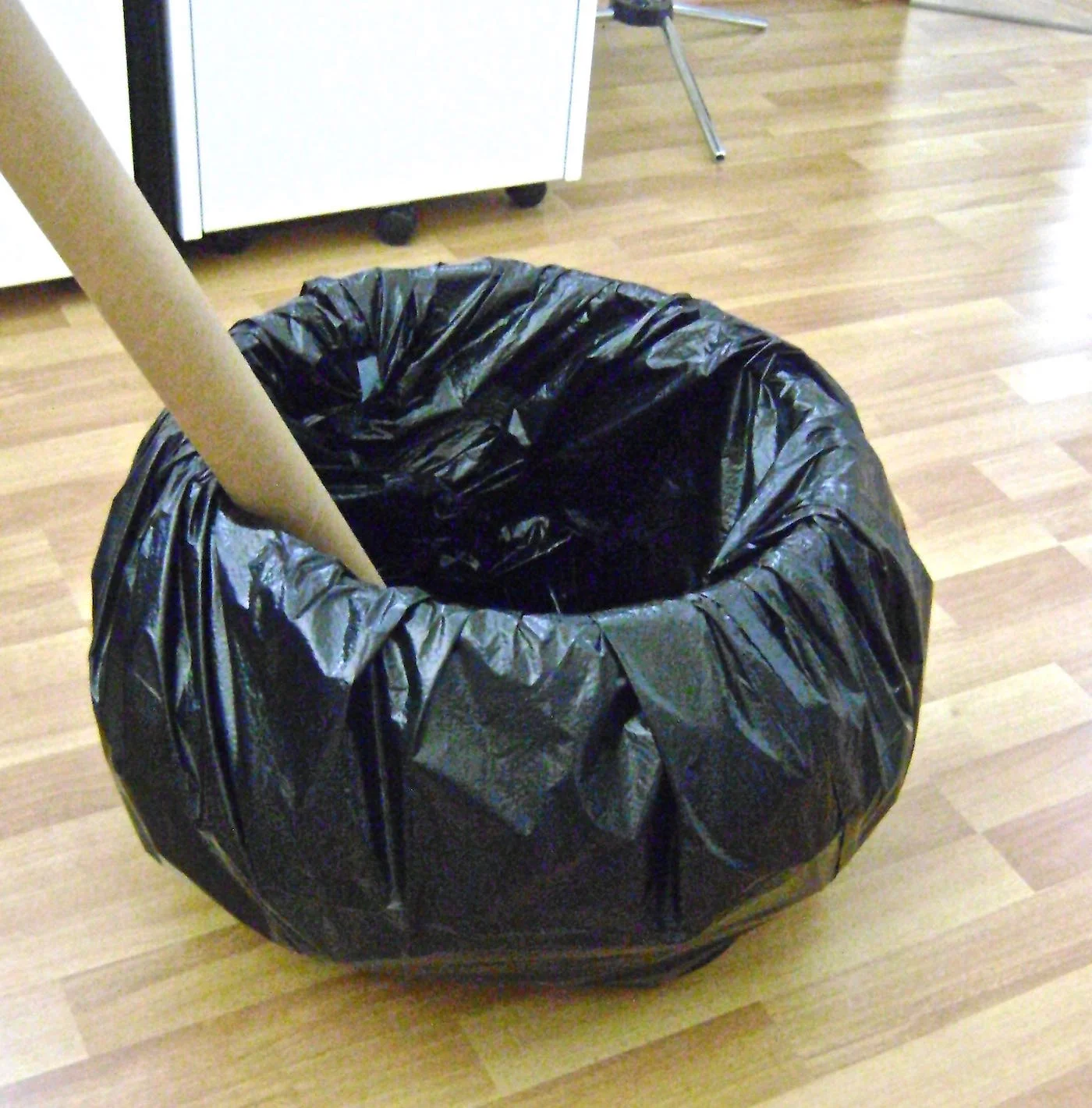 step 13 - Create the cauldron by setting a large planter, bucket or other container into a jumbo trash bag. Stuff crumpled newspaper between the bag and container to achieve a more rounded look. Stuff the bag top inside. Tape in place if necessary. Use a mailing tube wrapped in orange plastic as the witches stirrer. 