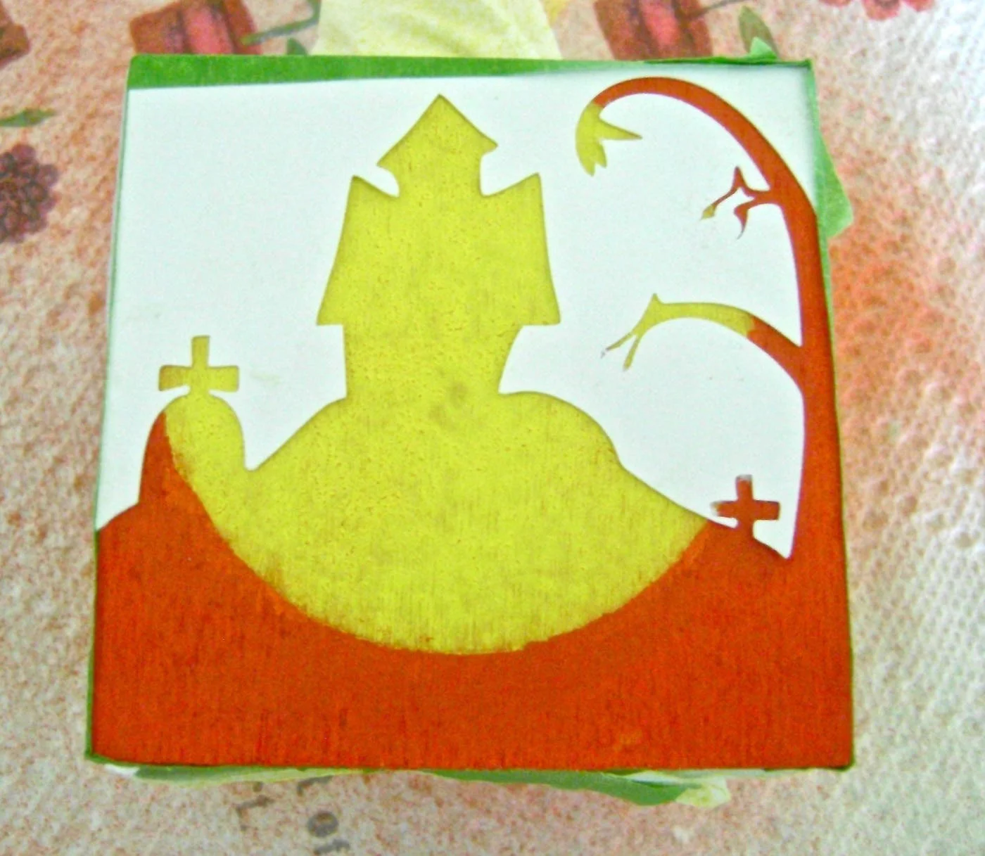 step 5 - When the yellow paint is dry, spray the back of the haunted house stencil with adhesive and press it to the cube matching up top and side edges. Airbrush the open area with black paint.