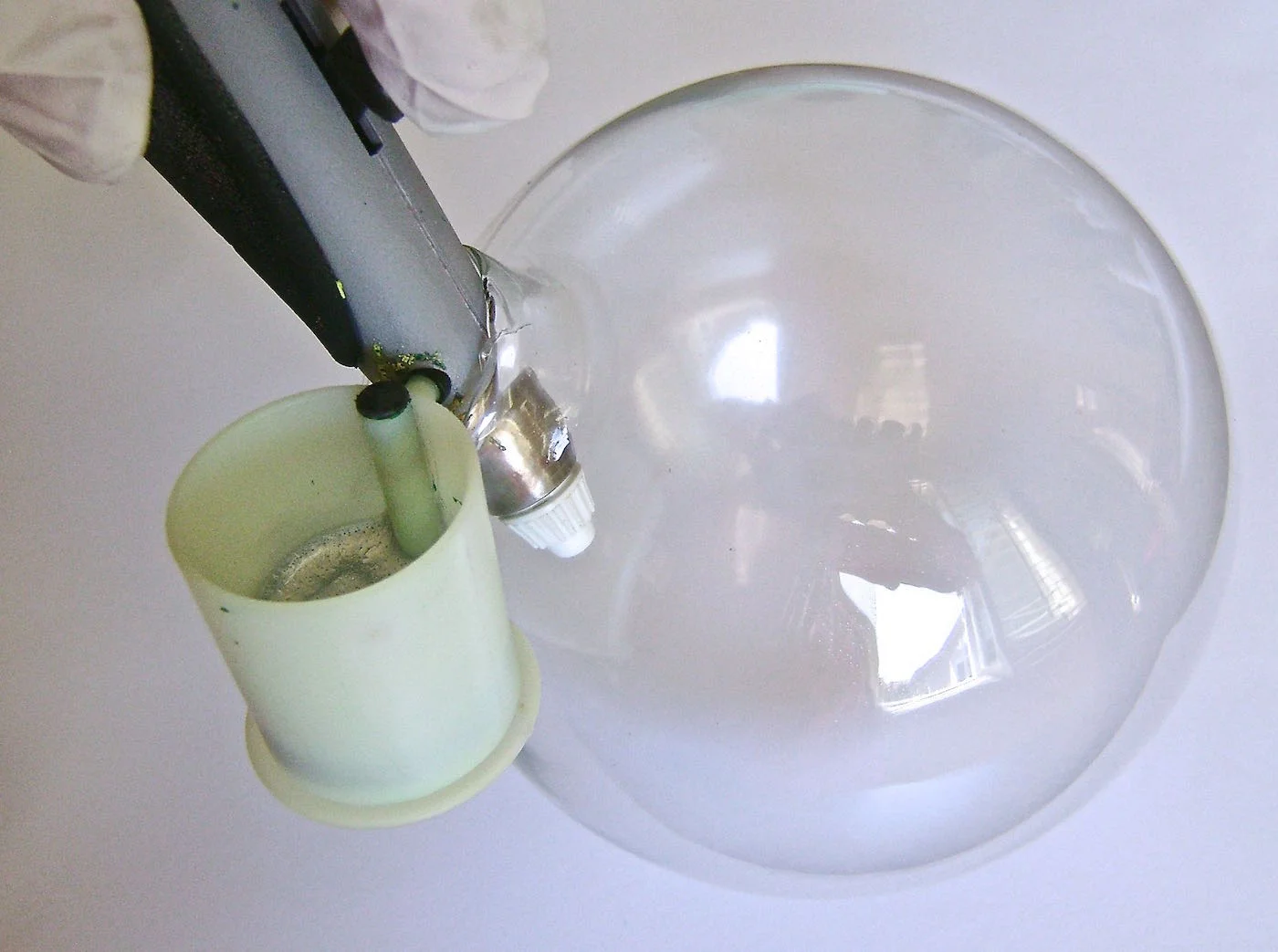 step 1 - Remove the metal hanger from the glass ornament. Fill the paint cup with the silver paint. Insert the airbrush into the ball opening. Spray a very light coat of paint inside. Turn the ball to reach the sides. Stop often and hold the ball up to the light to see how heavy the coating is. It won’t require much for a smoky effect.