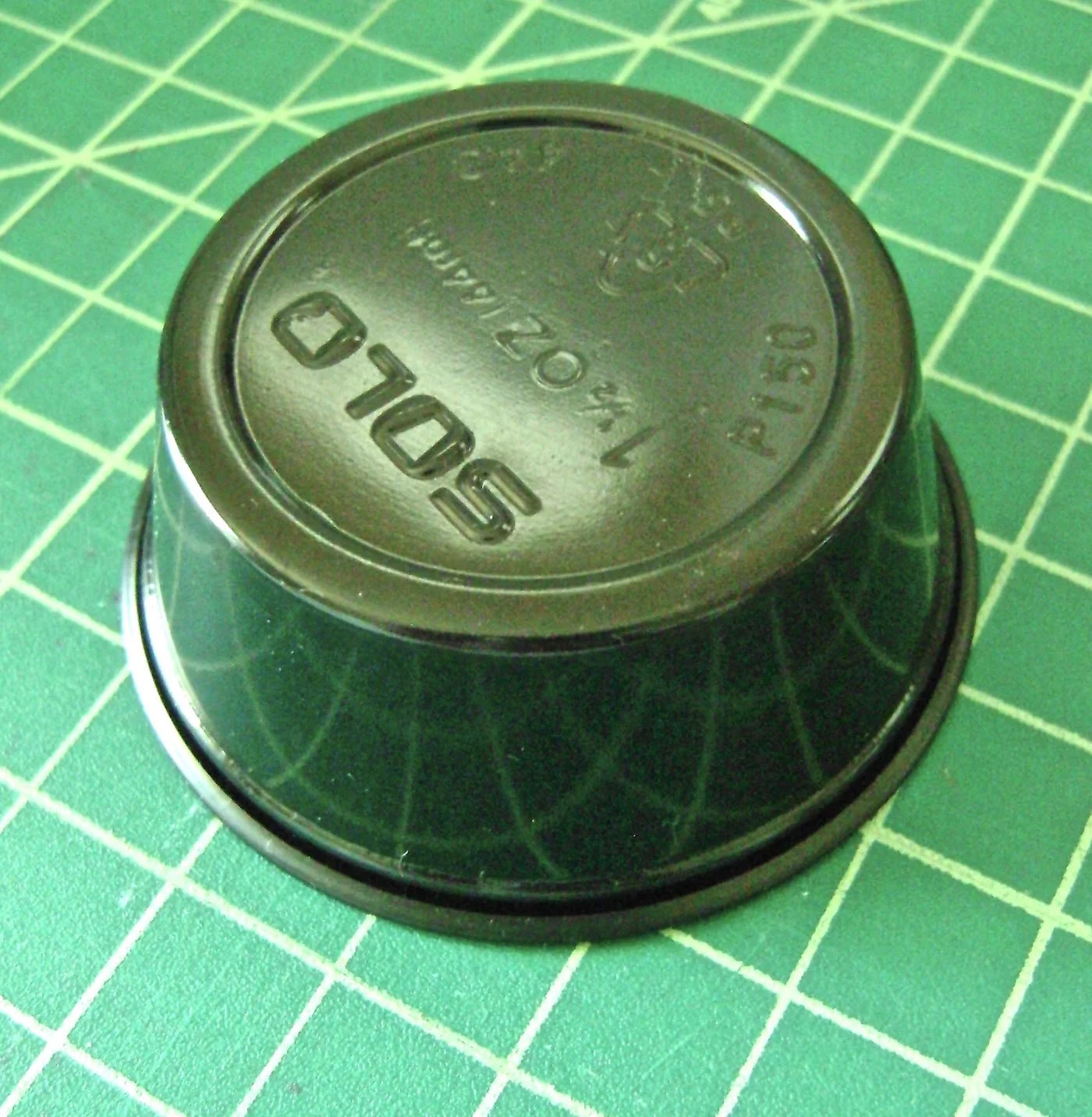 step 11 - Apply two beads of hot glue to the bottom of a small black condiment container. Place the centerpiece on the container with the card stock touching the glue.