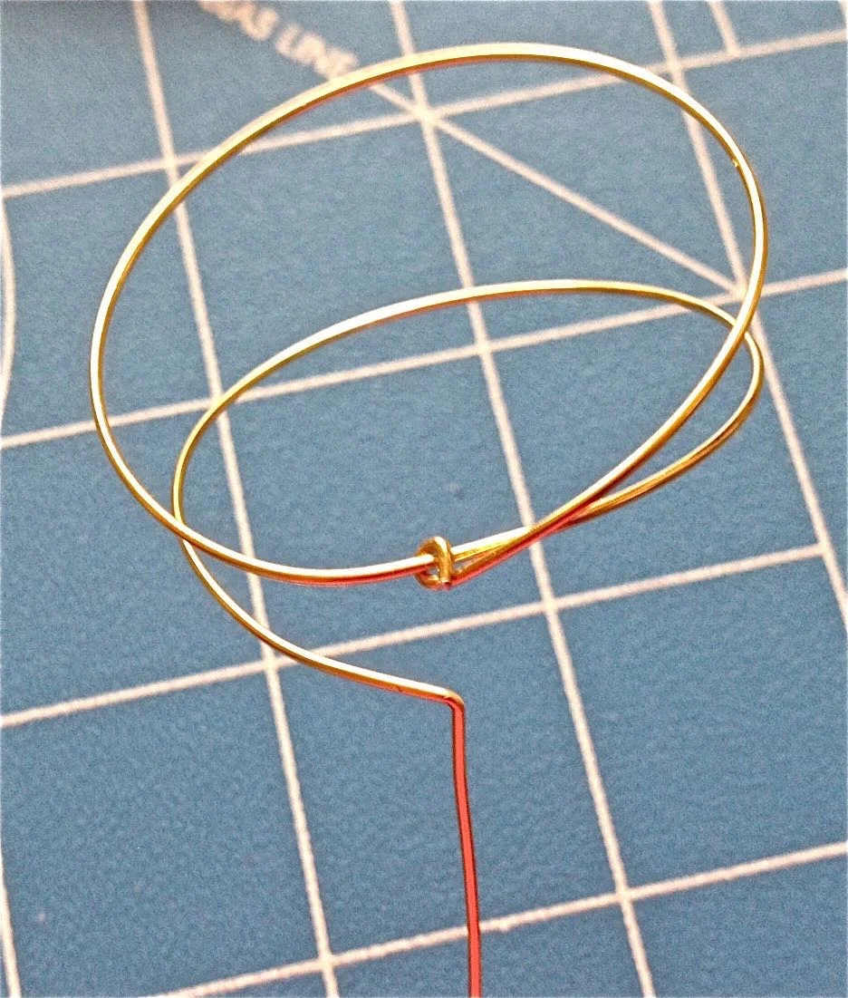 step 24 - Bend an angle in both wire ends and smooth them out so they’re straight. One should have a long stem, the other, a tail only long enough to make a small loop and attach it to the circle. 