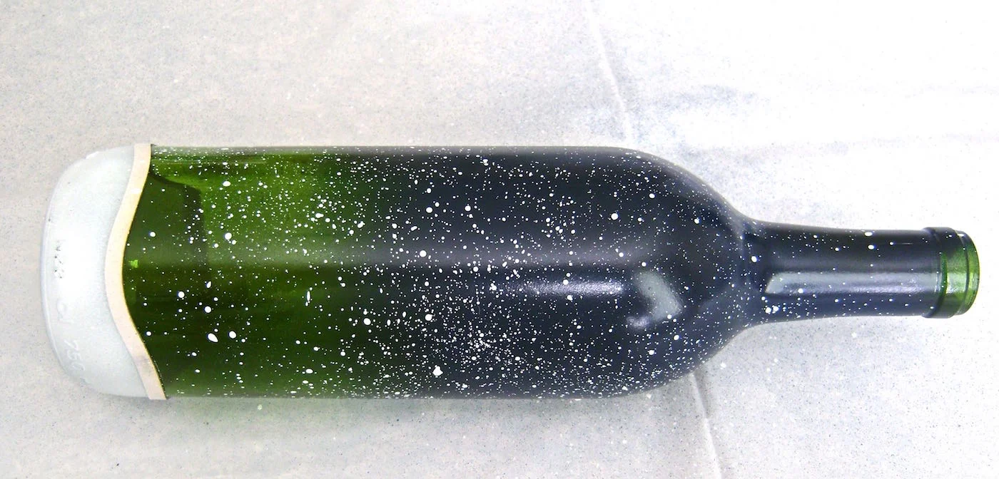step 5 - Add snow to the bottle. Dip an old soft bristled toothbrush in white paint. Tap the brush into paper towels or a rag to remove excess paint. Hold the brush a few inches from the bottle and with a gloved finger, flick the bristles to spray fine dots of paint on the glass.