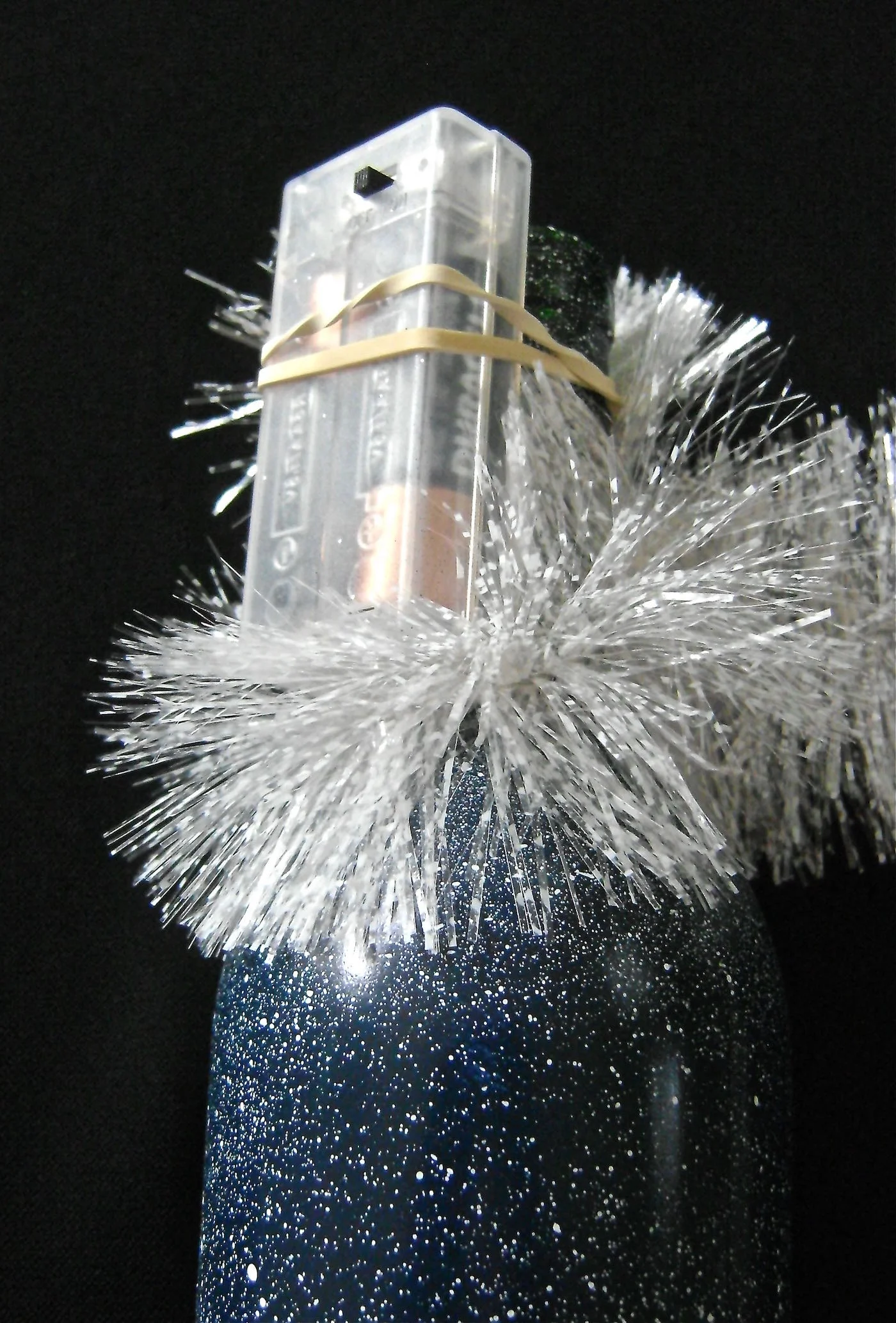 step 10 - Wrap a strip of white tinsel garland around the neck of the bottle to conceal the battery pack. Tuck one end into the rubber band and the other end into the bottle opening.