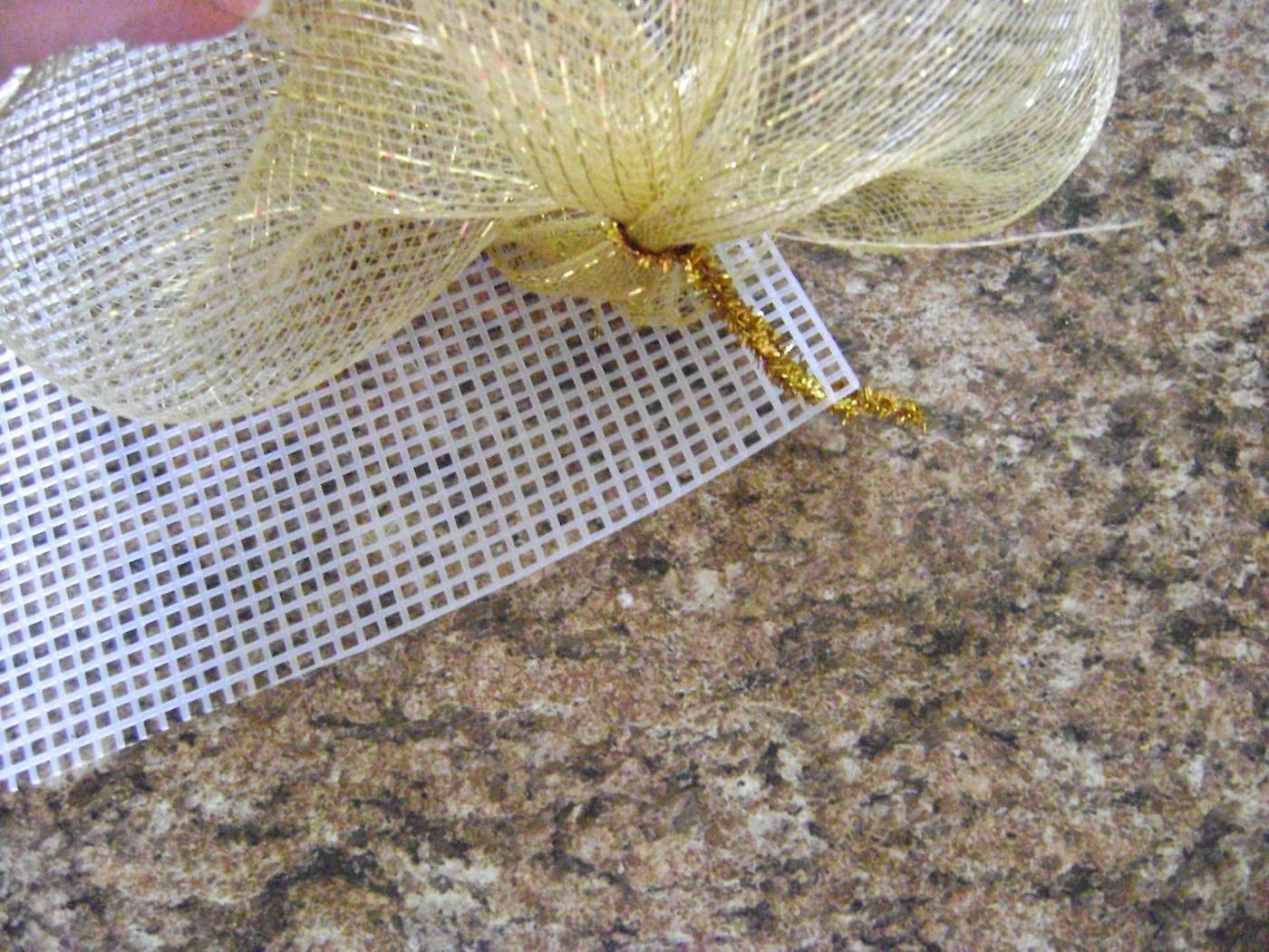 step 4 - When all the mesh on the roll has been gathered, push the first pipe cleaner through the corner holes of the canvas’ (13”) wide end. Twist the ends on the backside to secure the mesh to the canvas. Attach another four pipe cleaners across the top edge in a straight line about 2.5” apart. The fifth pipe cleaner should be placed in the opposite corner.