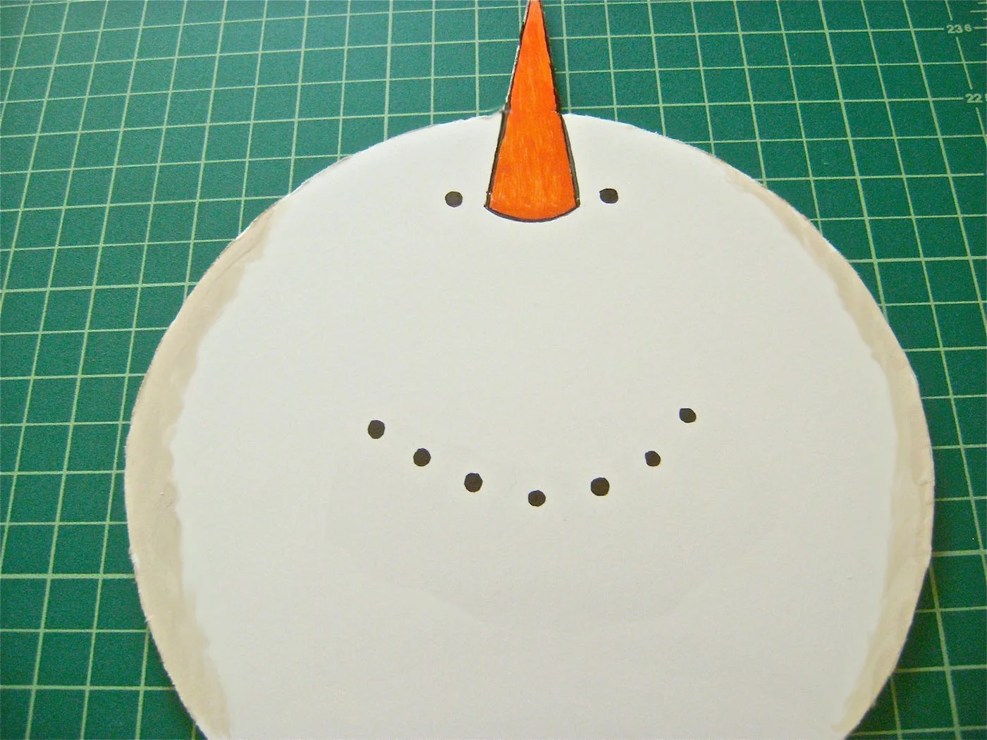 step 4 - Give the flat snowman dimension by outlining the edges of the face and body with tan paint. Apply paint, creating a curve between the middle and bottom circles. Cut a strip of mesh about 12” wide to create the scarf. Use hot glue to attach it to the foam board.