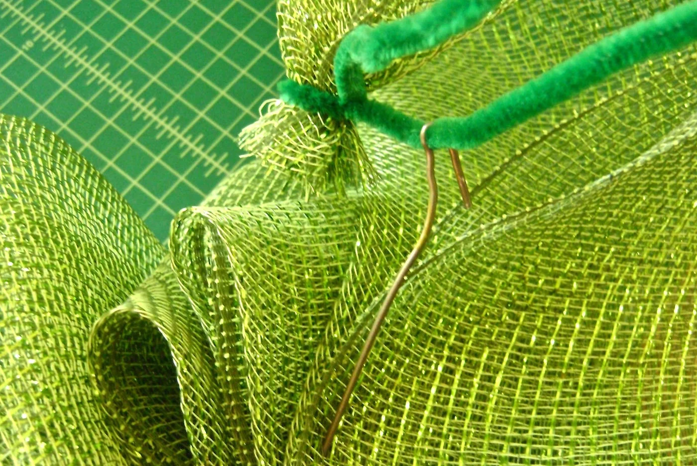 step 9 - Wrap a pipe cleaner around the mesh end. Attaching the pipe cleaner to the bend in the hanger wire which will form a loop in the 20”of the deco mesh and conceal the raw edge. Add deco mesh to the other side of the hanger in the same way.