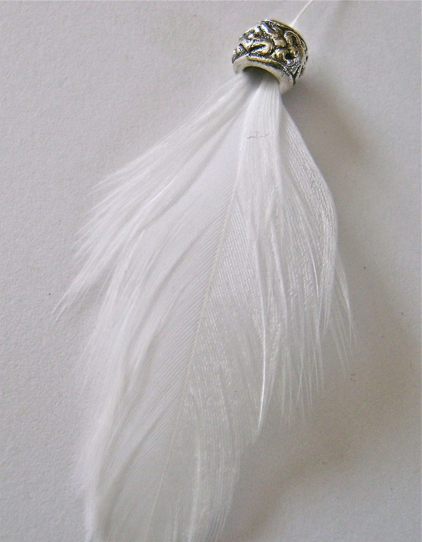 step 4 - Pass the feather’s quill through a decorative silver spacer and then into a 10mm pearl. Push the wire stem up into the spacer and through the pearl with the feather draped across the front side of the wings.