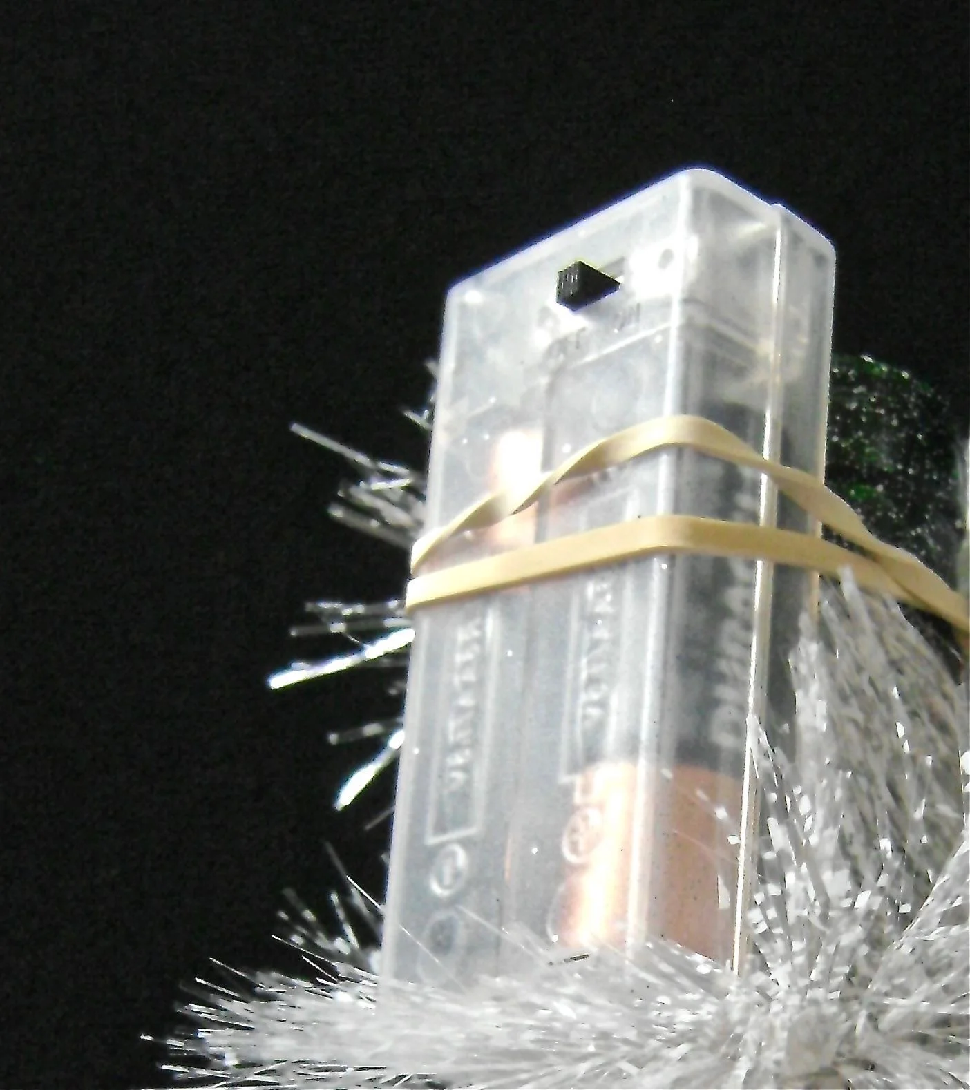 step 14 - Loosely stuff the lights into the bottle. Attach the battery pack to the neck of the bottle with a rubber band. The switch should be positioned so that it is easy to access. Wrap a strip of white tinsel garland around the neck of the bottle to conceal the battery pack. Tuck one end into the rubber band and the other end into the bottle opening.