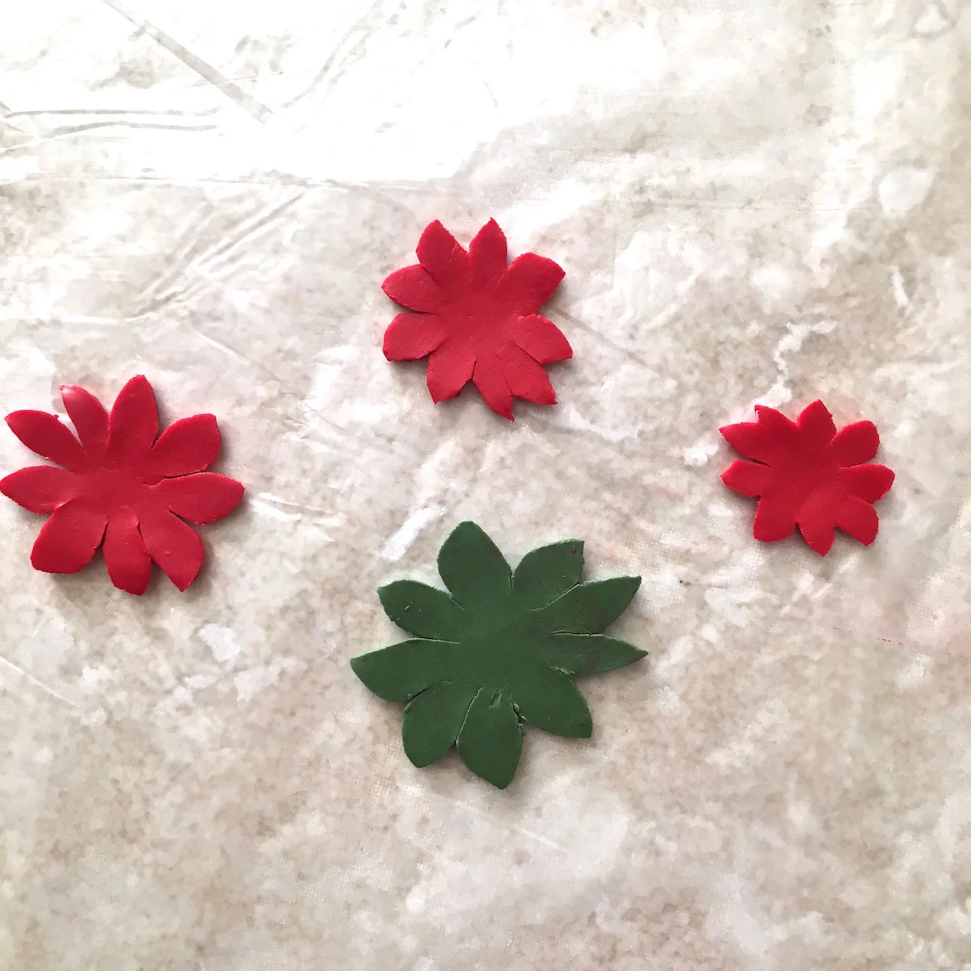 step 3 - You will be creating two poinsettias, one for the front of the ornament and one for the back. Each consists of a green base with three red layers stacked on top. Use the card stock stencil to cut out two green clay pieces from the largest shape. Cut two red clay pieces for each of the three remaining shapes.
