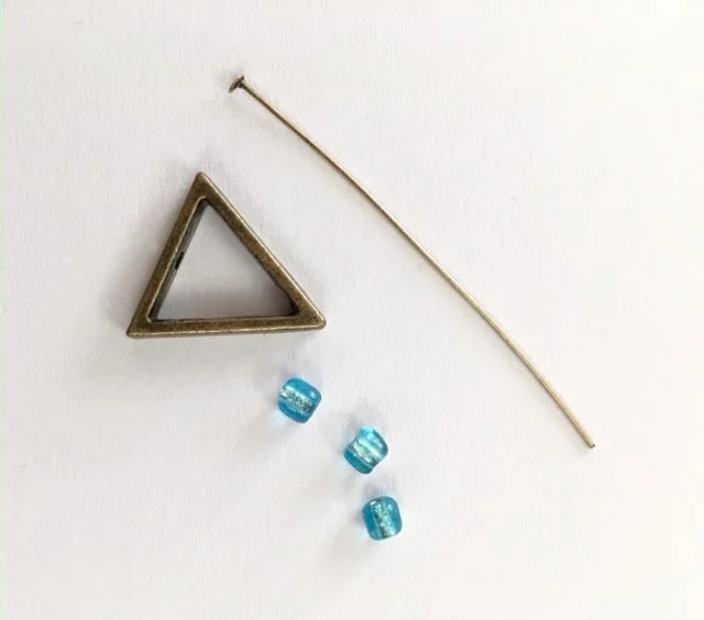 step 1 - Each triangle element requires a triangle, a nail head wire, and three beads. There are holes in the triangles on the pointy end and the opposite straight edge. Insert the nail head wire into the pointed end of the triangle frame.