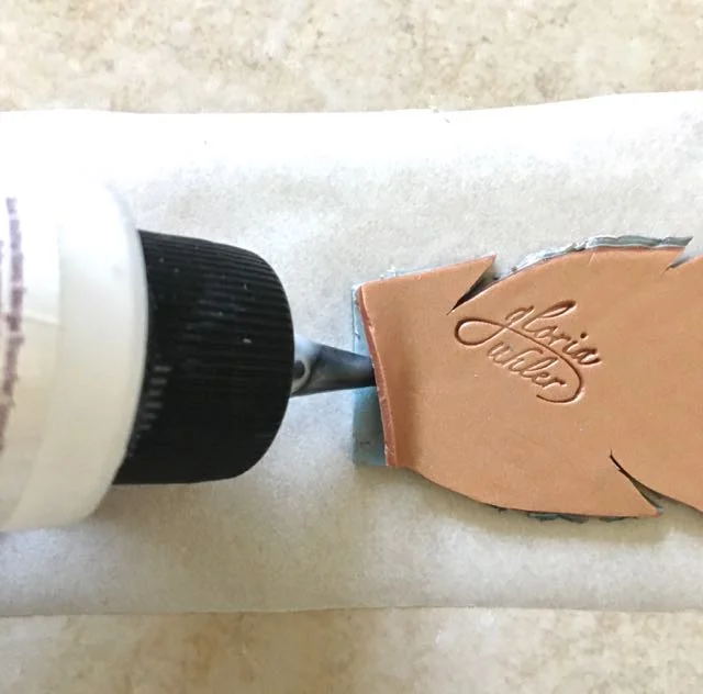 step 19 - Position one feather right side down on a 4" wide strip of parchment paper. Apply liquid polymer clay between the two layers on the straight edge of the feather.